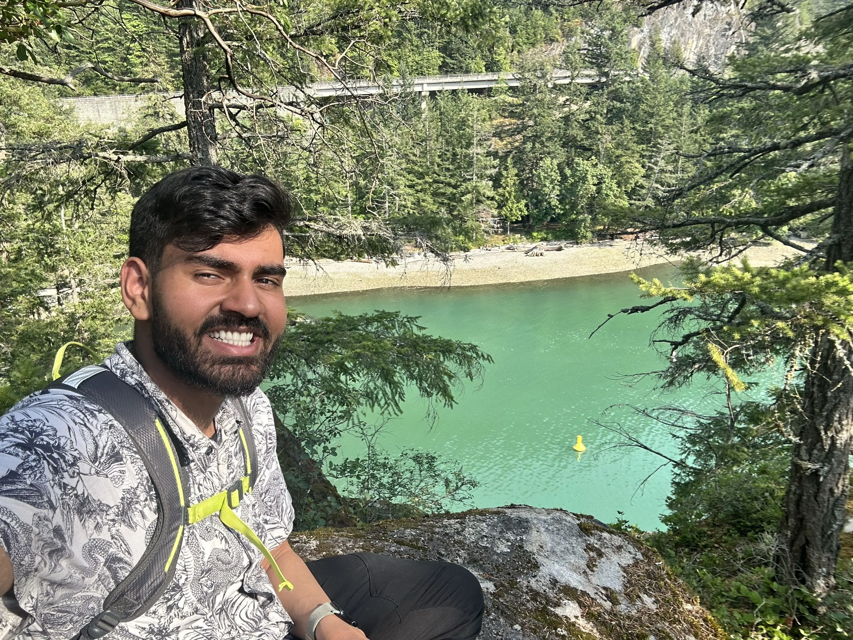 Smiling selfie on a rock above turquoise water and forest